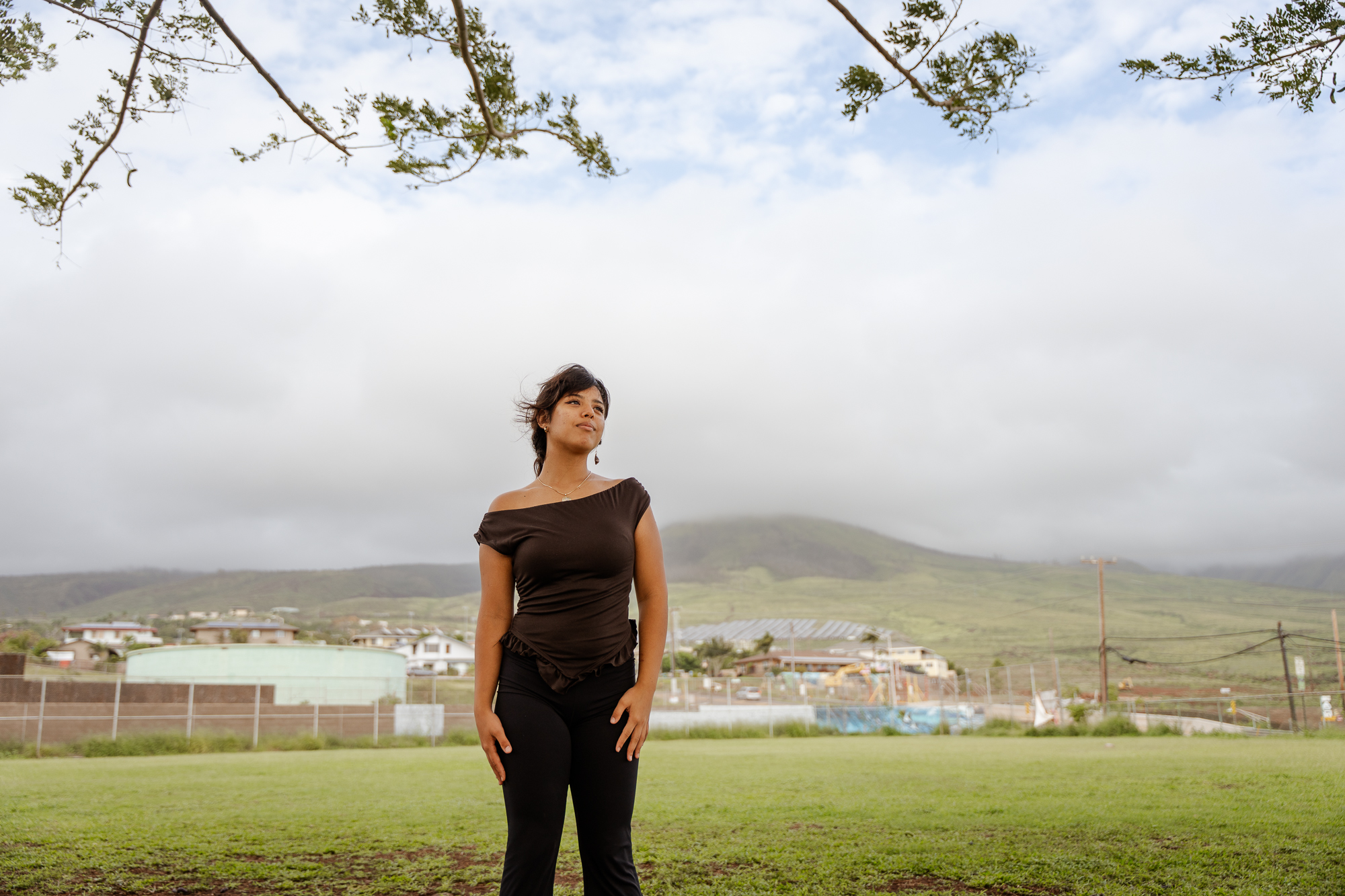 A young woman, Mia Palacio, stands in a park in Lahaina with Mt. Ball in the background.